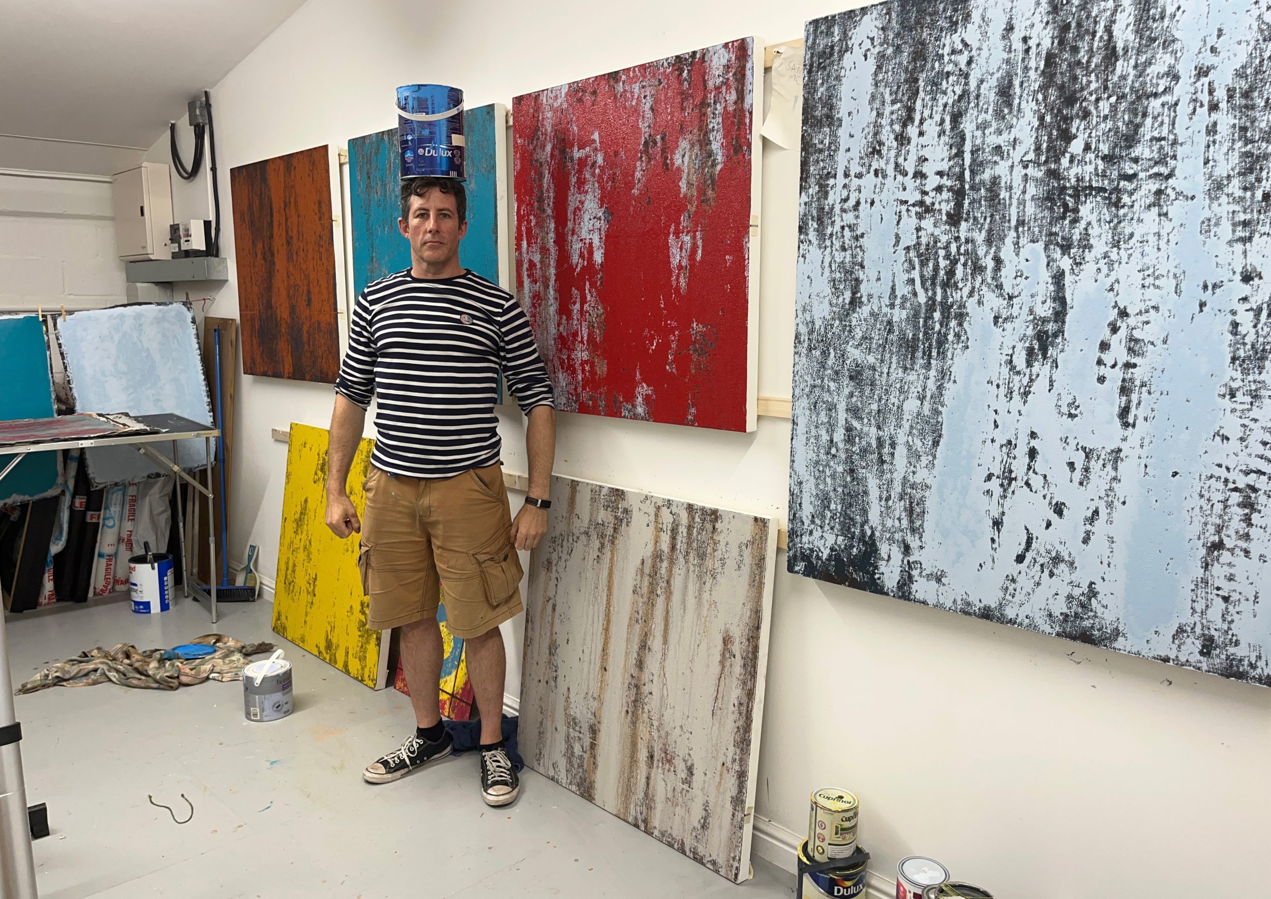 A photo of award winning artist Joe Hodway balancing a can of paint on his head. 